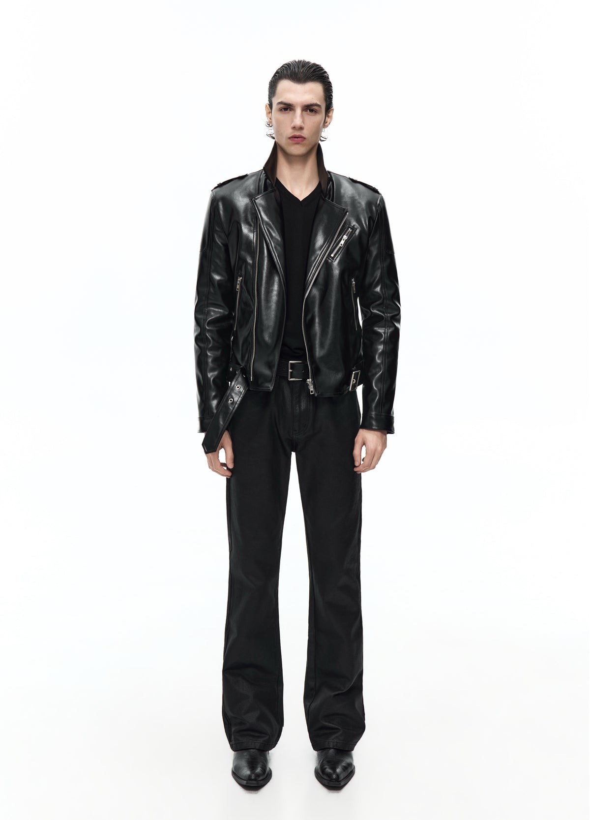 Front view of a model in a shiny black biker jacket worn open, showing wide lapels and silver-tone zips above black trousers.