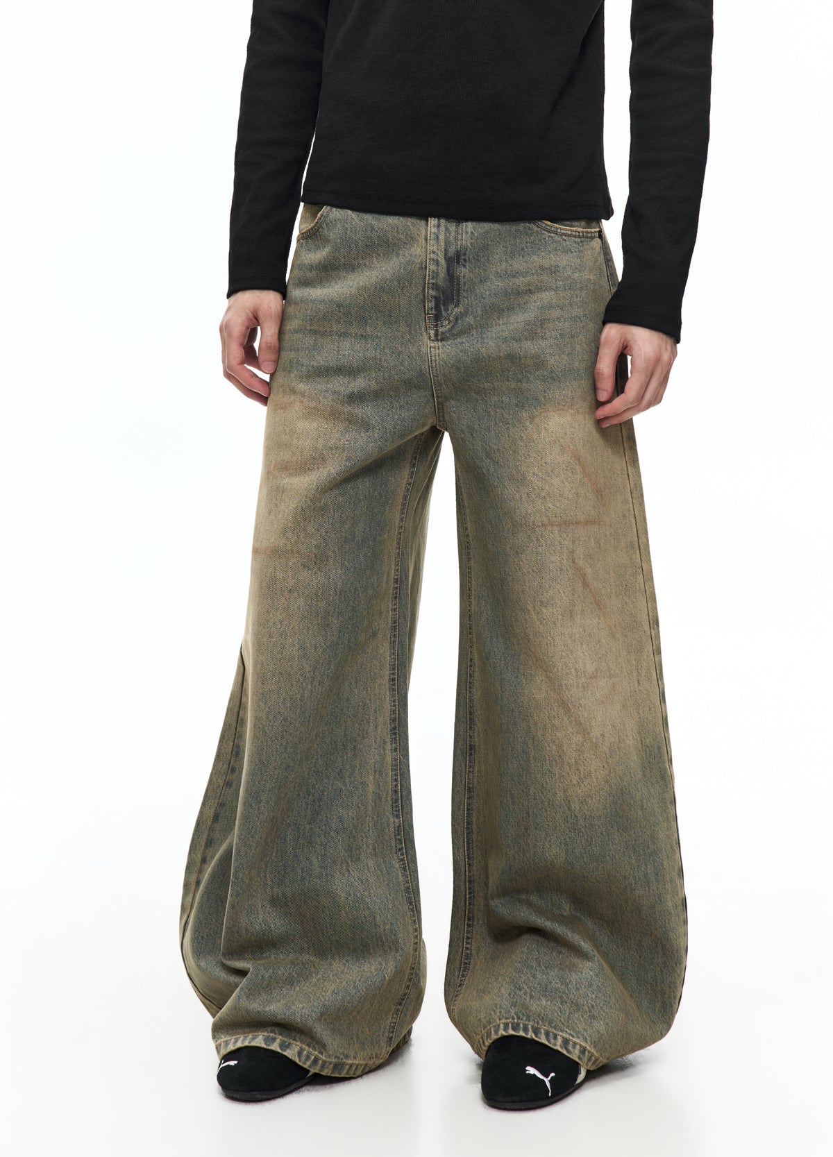 Front view of very wide washed jeans from the waist to the shoes, showing a faded green-brown appearance and curved seams down the legs.