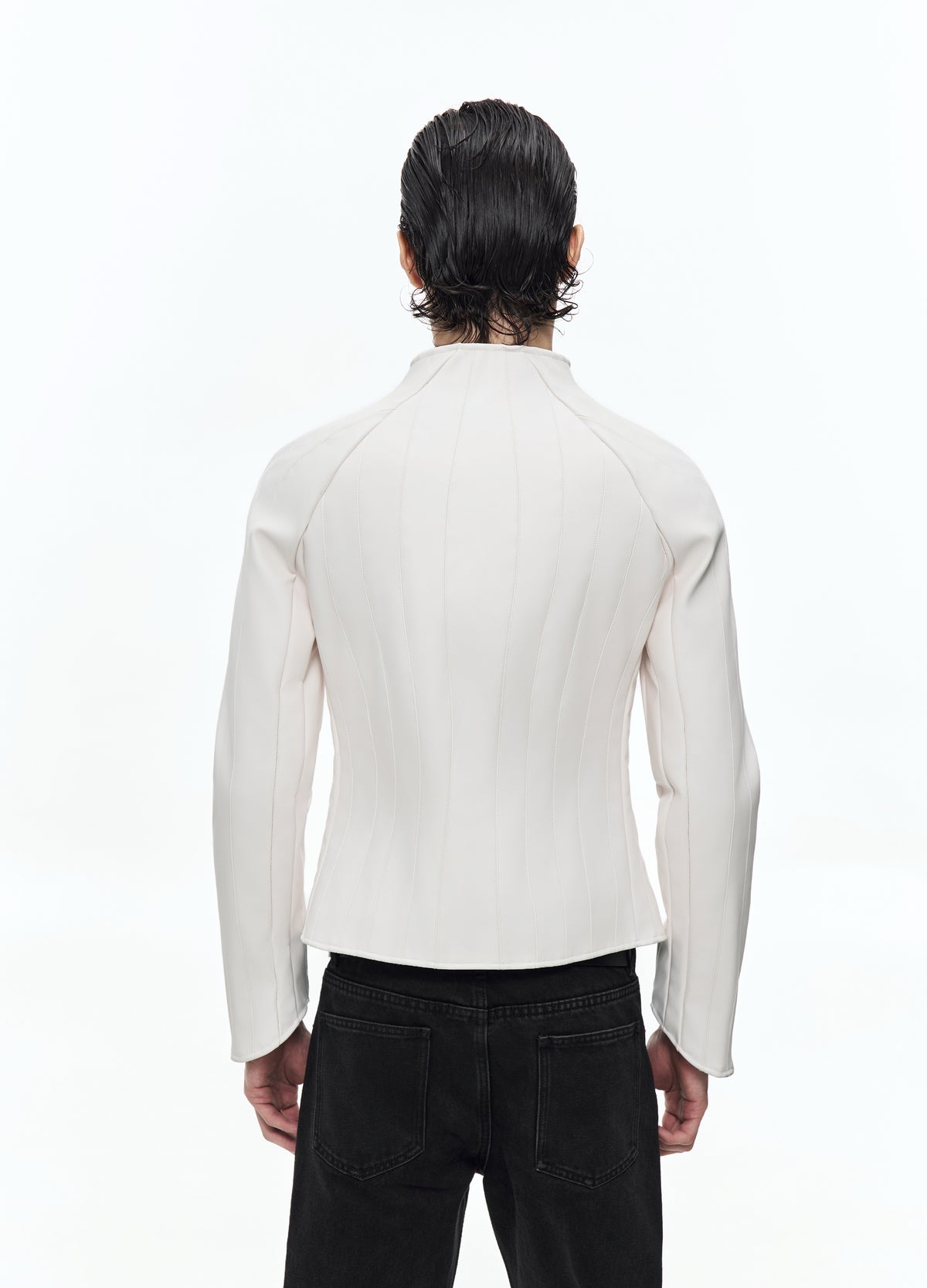 Rear view of the off-white jacket, showing curved vertical seams, long sleeves and a fitted waist above black trousers.