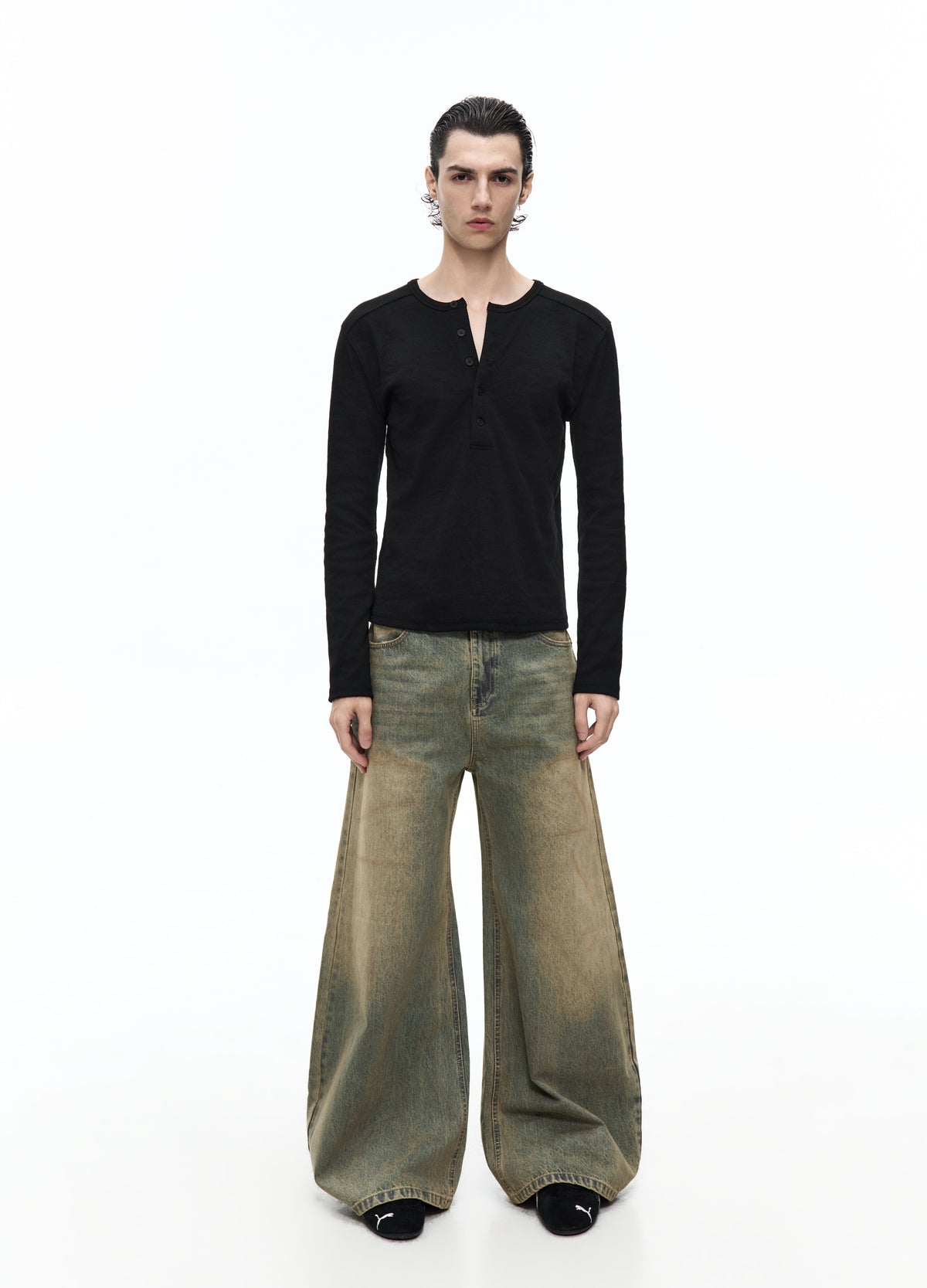 Full-length view of a model in very wide washed jeans with a fitted black long-sleeve top and black shoes.