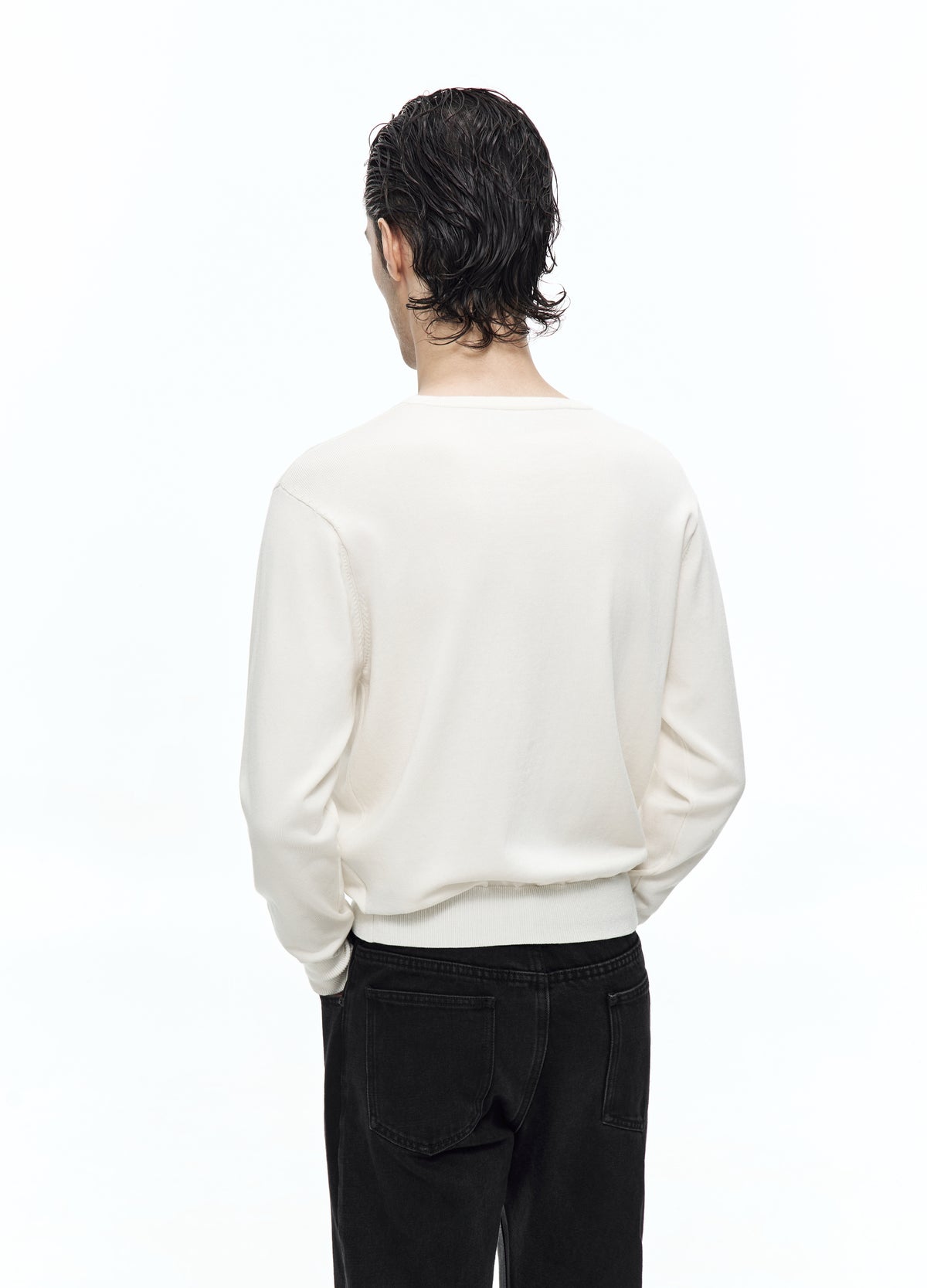 Rear view of the off-white top, showing its plain back, long sleeves and gathered hem above black trousers.