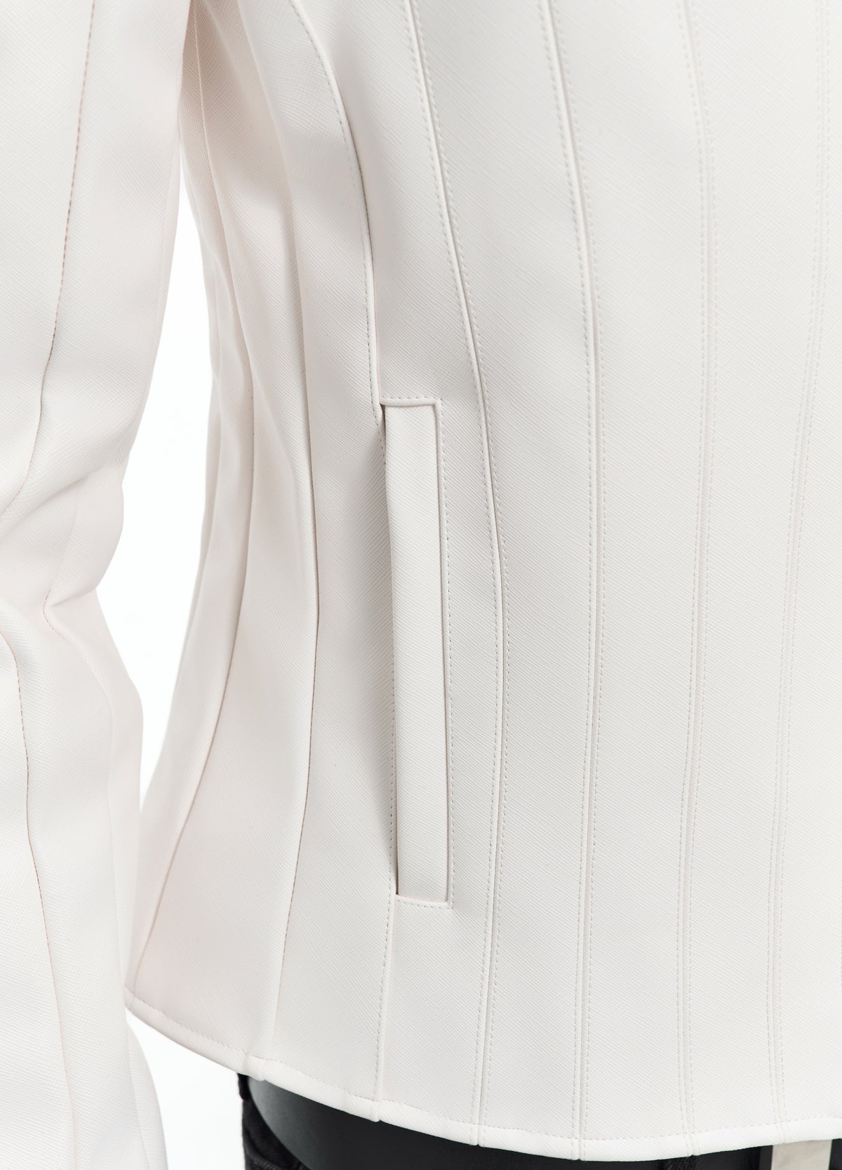 Close-up of the off-white jacket at the waist, showing parallel vertical stitching, the narrow pocket opening and curved hem.