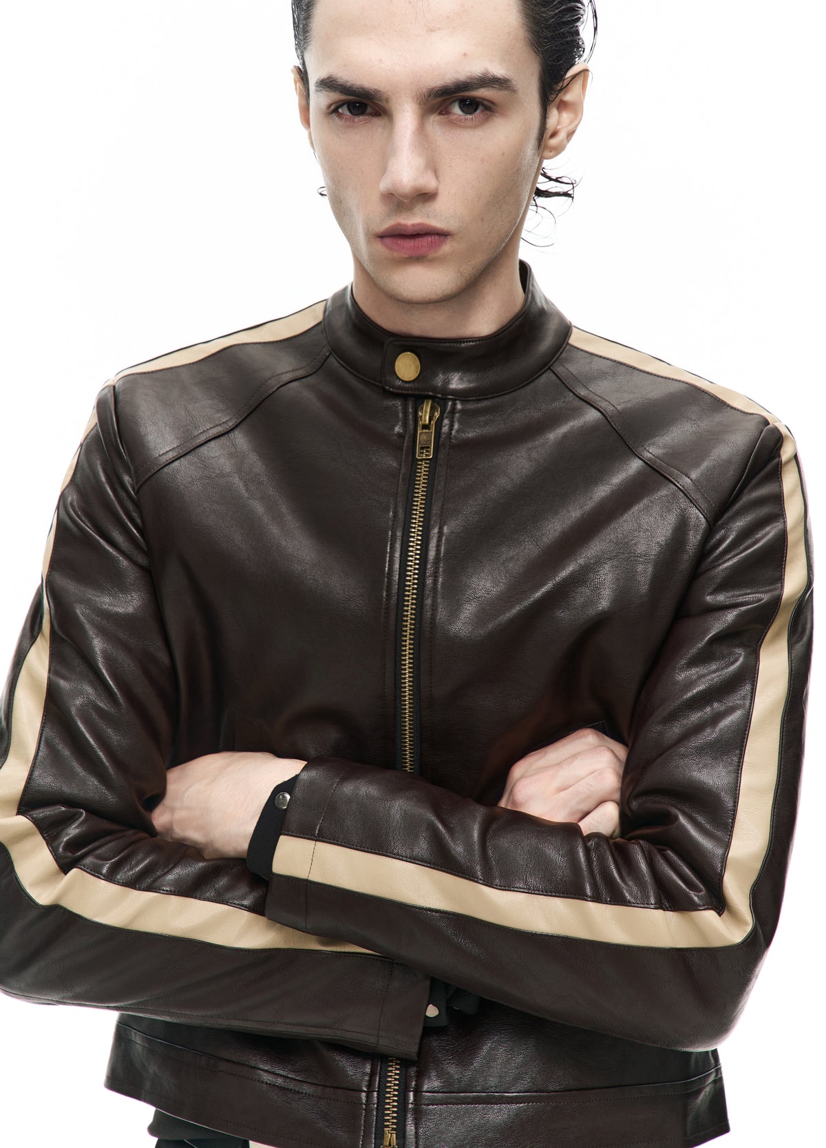 Close view of the dark brown jacket with folded arms, showing the collar snap, central zip, panel seams and pale sleeve stripes.