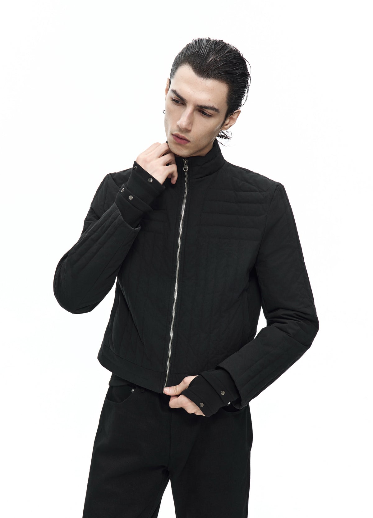 Closer front view of the black quilted jacket zipped up, with one hand at the stand collar and the other near the hem.