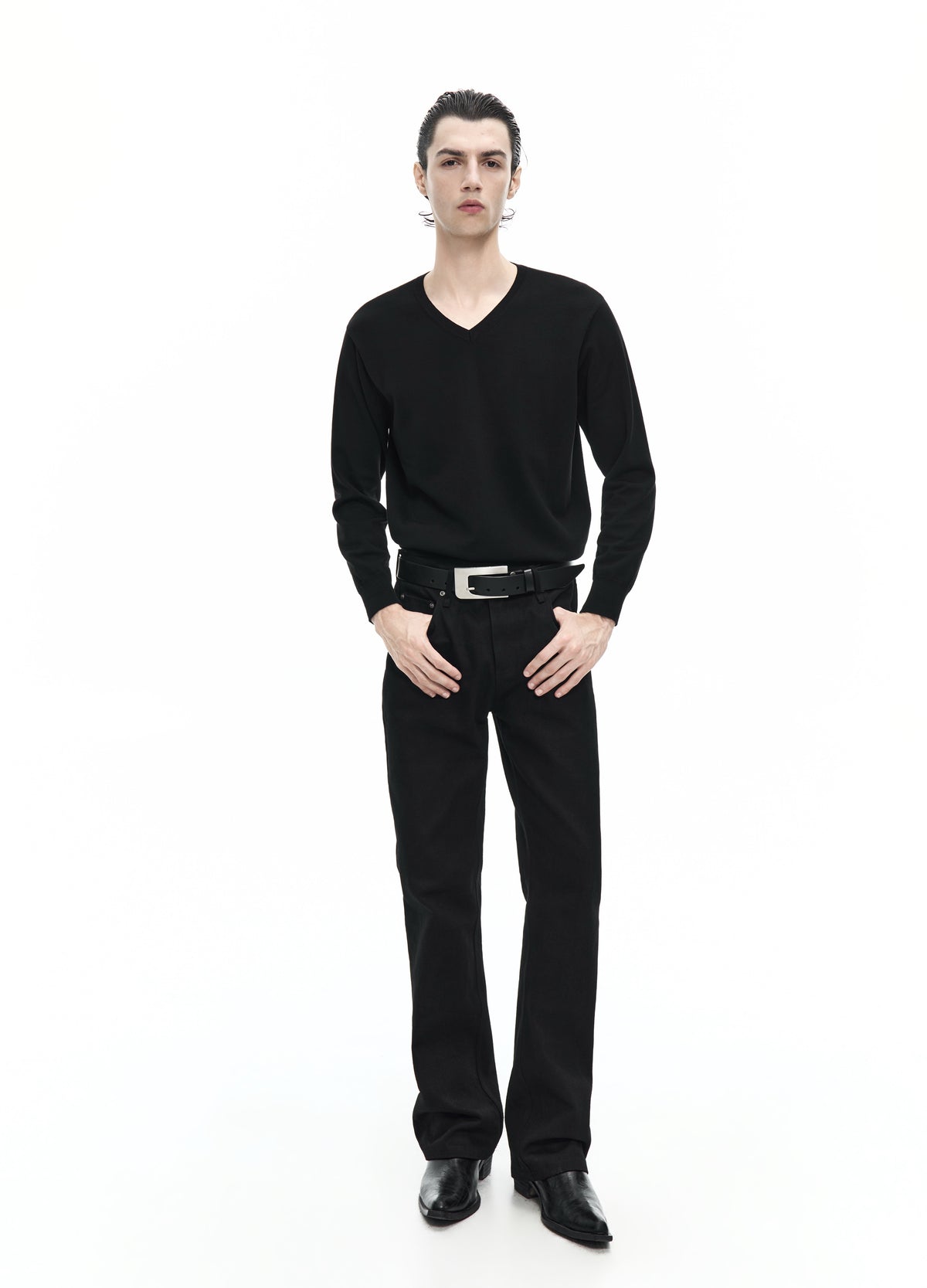 Full-length view of a model wearing straight black jeans with a black V-neck top, belt and black shoes.