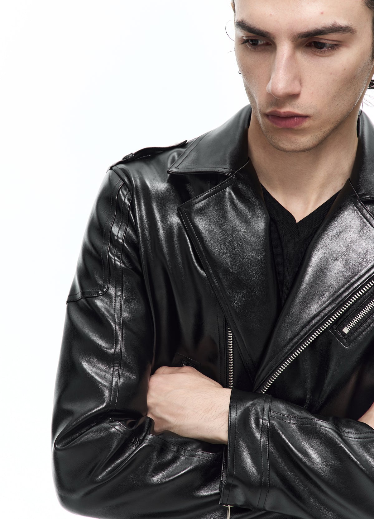 Close view of the black biker jacket with folded arms, showing the lapel stitching, diagonal zip and glossy folds in the sleeves.