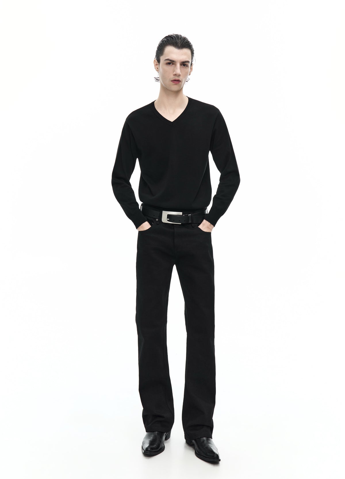 Front view of a model in a black V-neck top with long sleeves, worn with a belt, straight black trousers and black shoes.