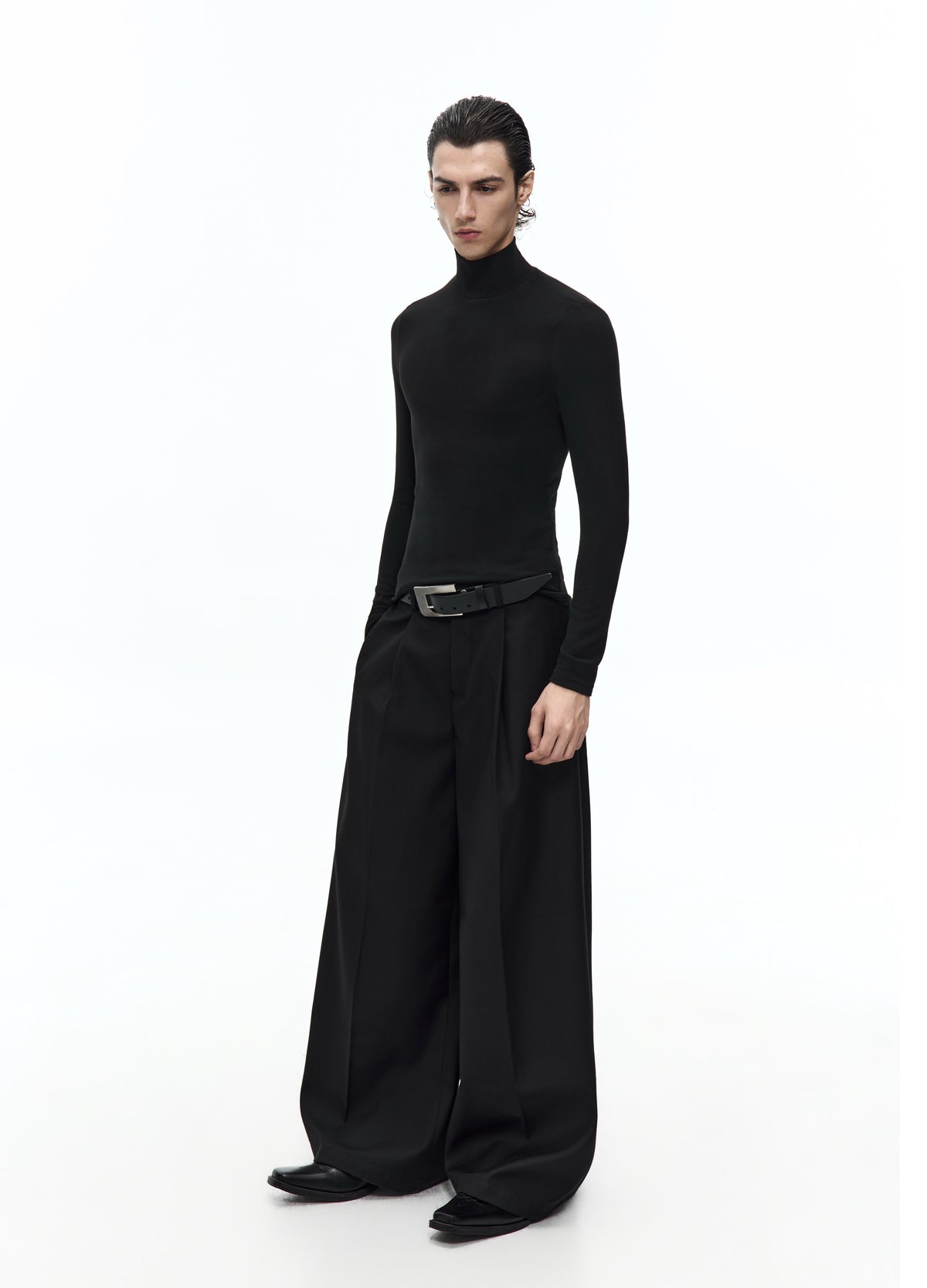 Three-quarter view of the fitted black high-neck top, showing the slim sleeves and waist above wide pleated black trousers.