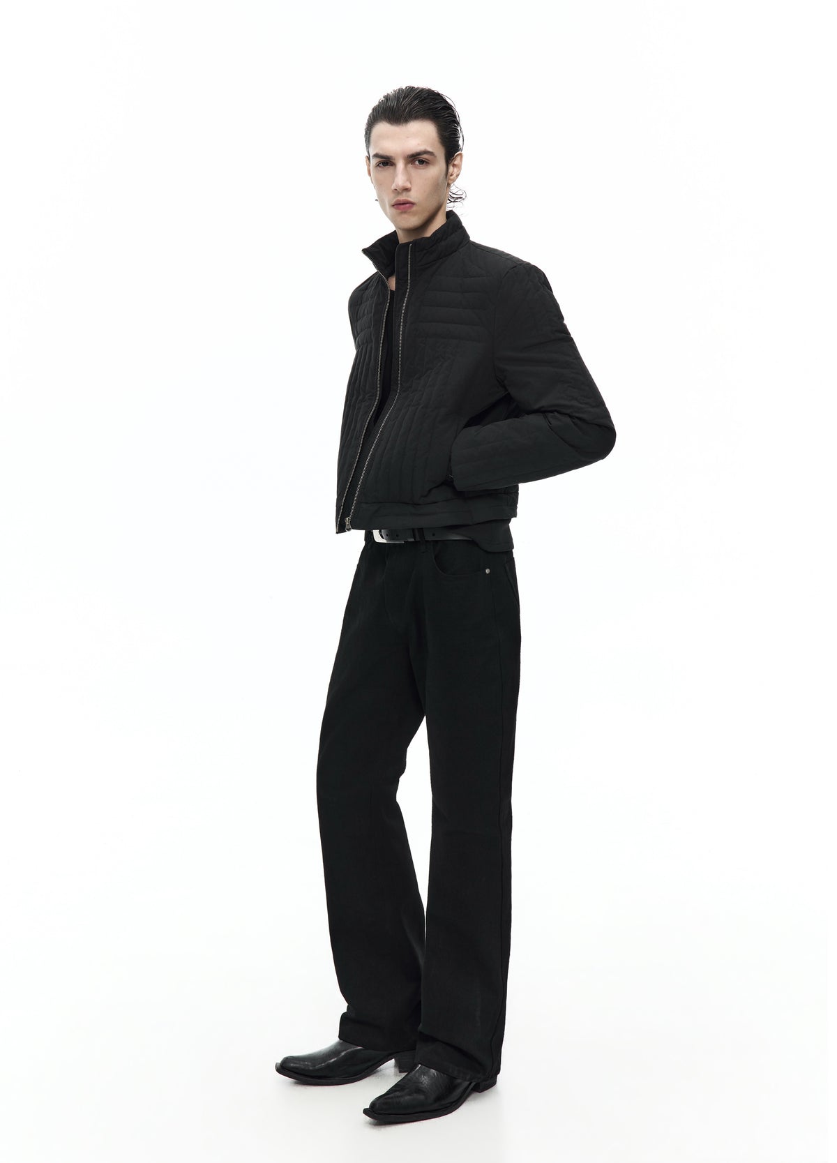 Side view of the short black quilted jacket, showing the raised collar, padded sleeve and a hand in the side pocket.