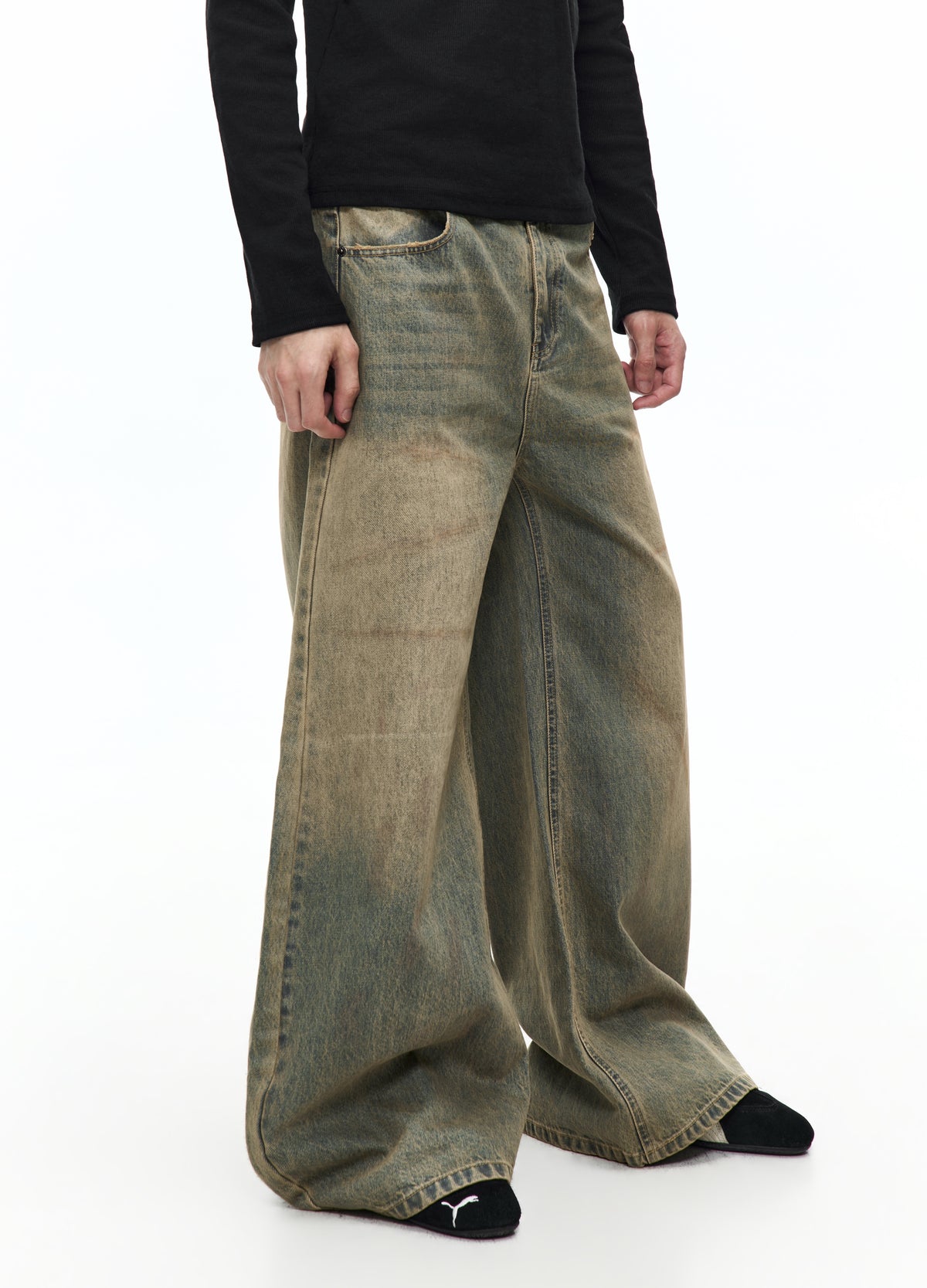 Three-quarter view of the very wide washed jeans, showing the faded front, curved side seams and long hems over black shoes.