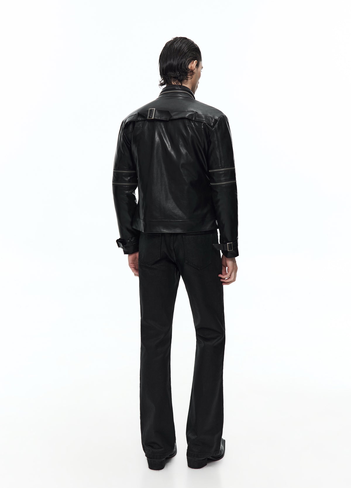 Rear view of the black jacket, showing the upper-back strap, sleeve zips and buckled cuffs above black trousers.