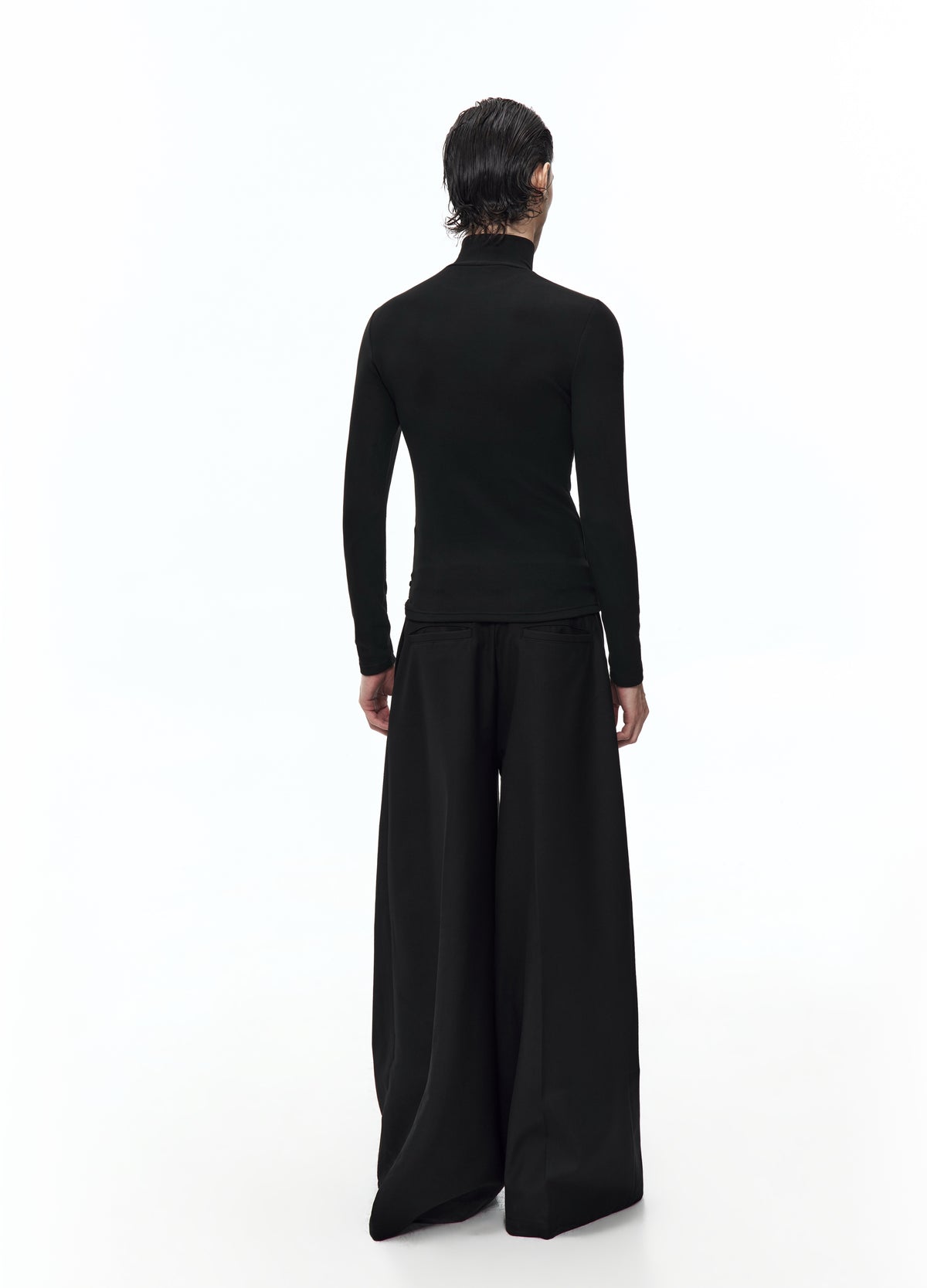 Rear view of the fitted black high-neck top, showing its plain back and long sleeves above very wide black trousers.