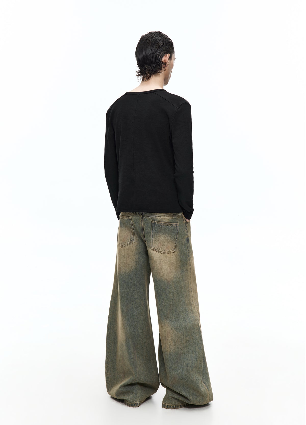 Rear view of the very wide washed jeans on a model, showing two back pockets, faded areas and loose hems near the floor.