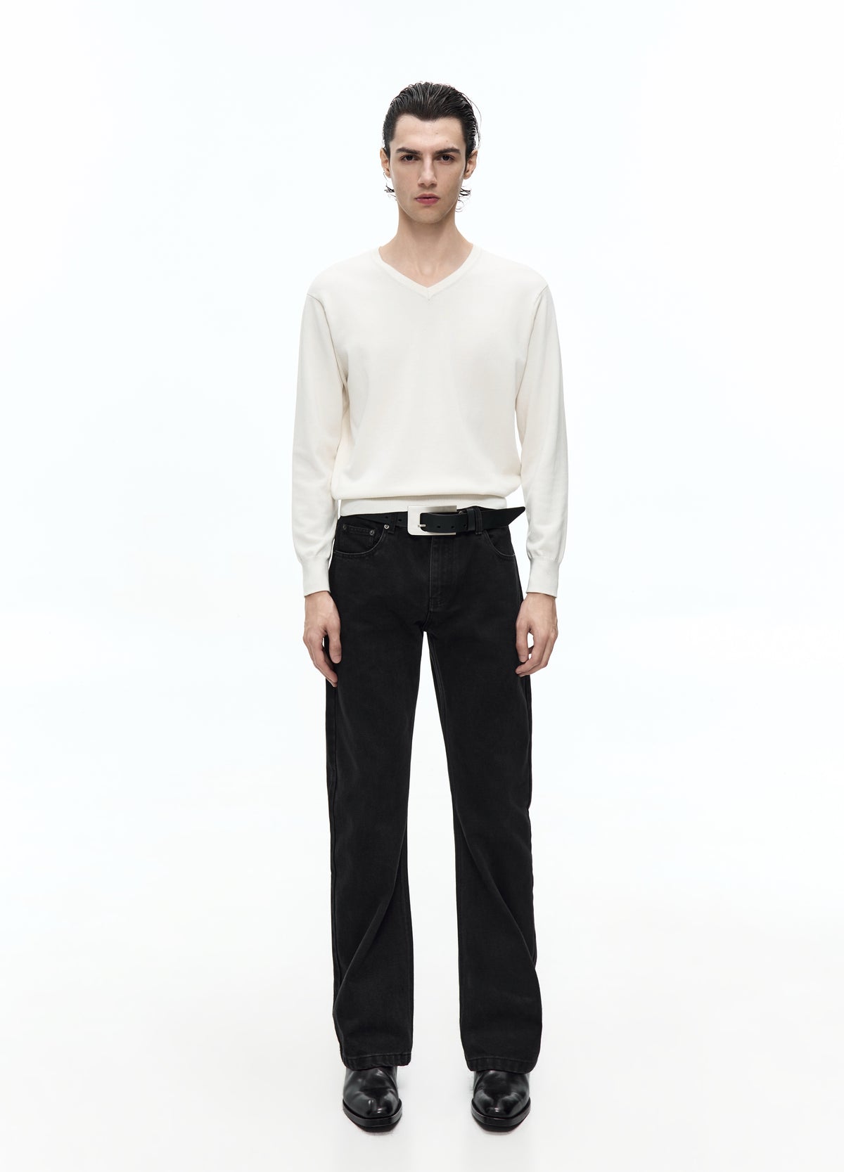 Front view of a model in an off-white V-neck top with long sleeves, worn with a black belt, trousers and shoes.