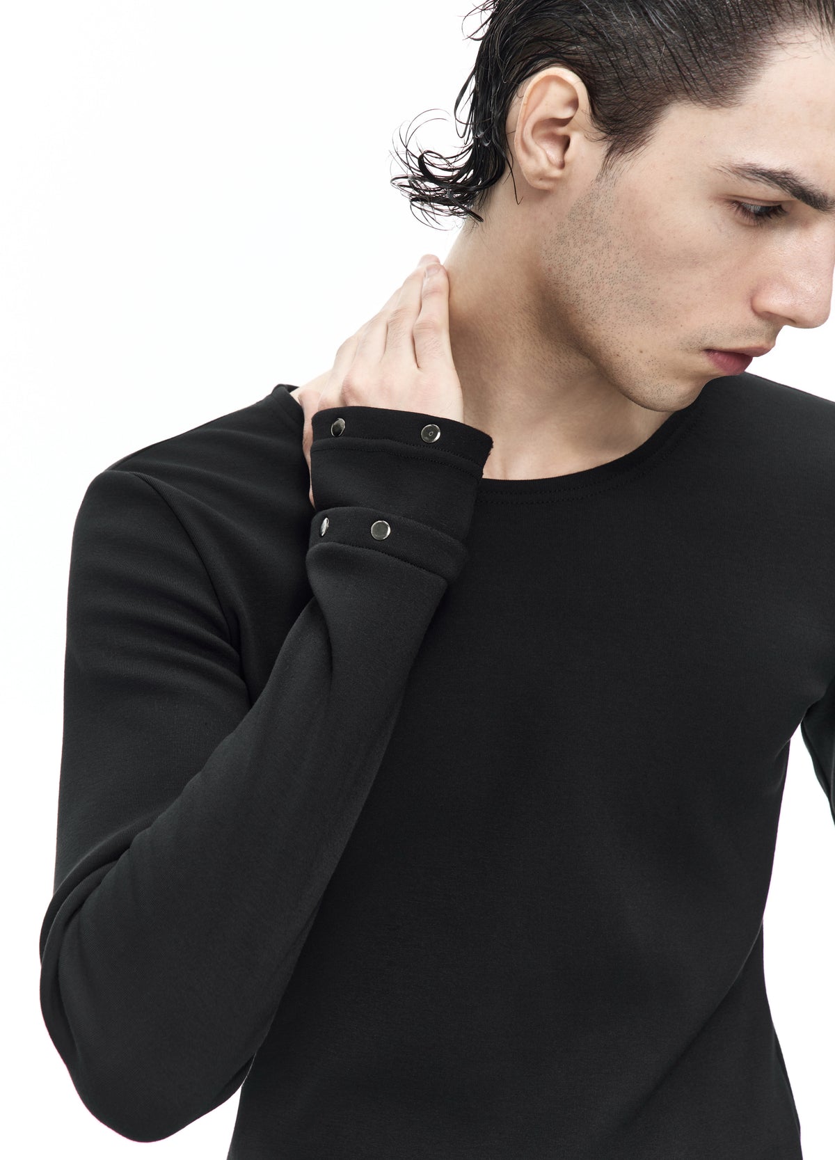 Close view of a raised sleeve on the black top, showing layered cuffs with small round metal details beside the round neckline.