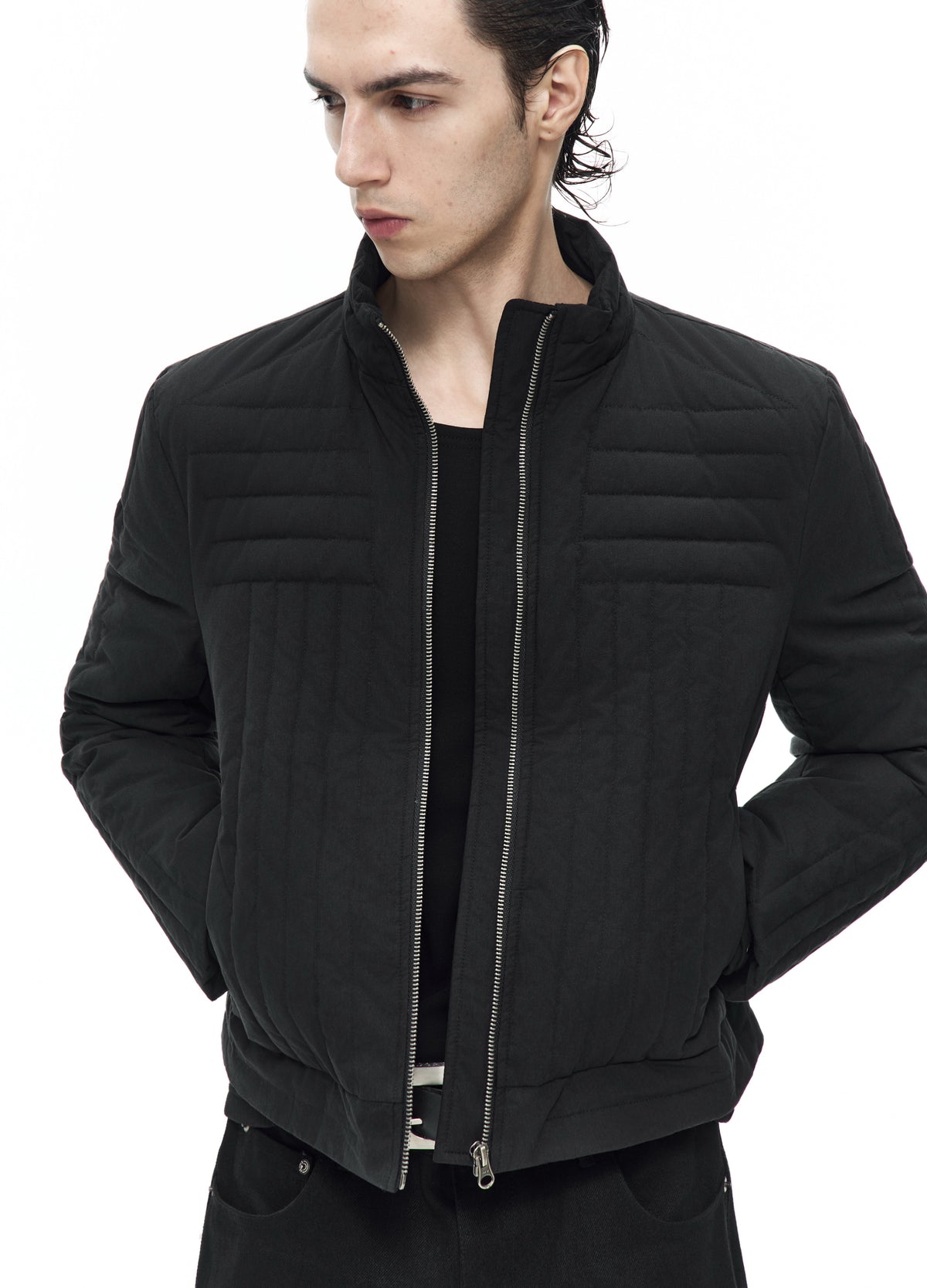 Close front view of the open black quilted jacket, showing horizontal chest channels, vertical lower stitching and the central zip.