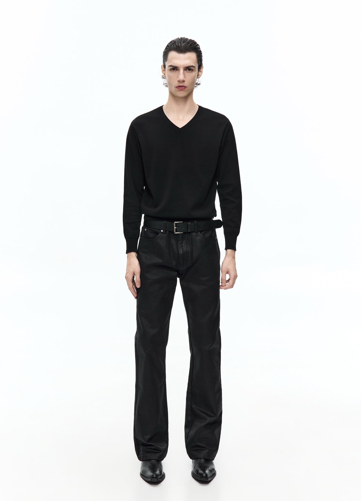 Full-length view of a model wearing glossy black trousers with a black V-neck top, belt and black shoes.